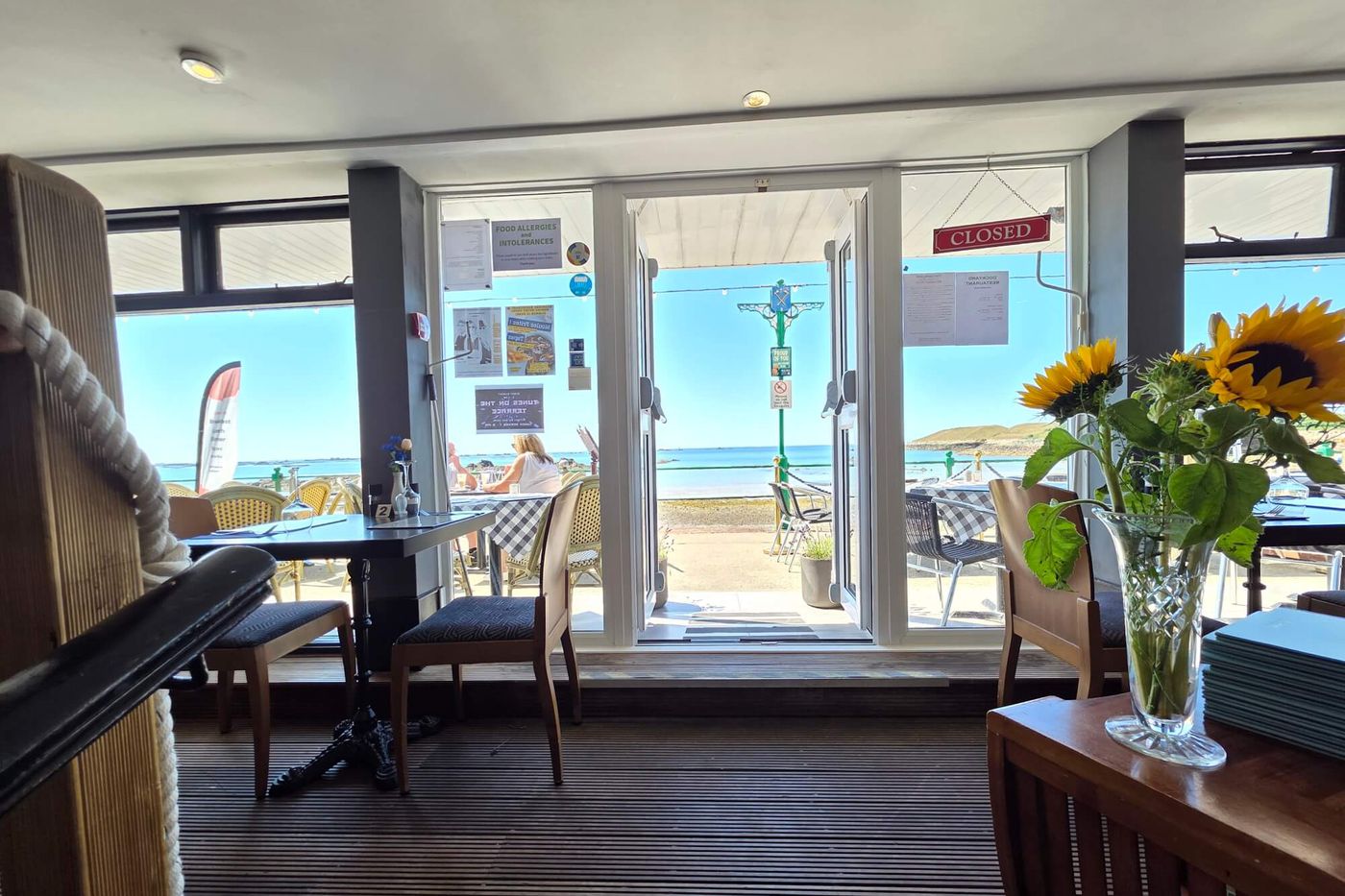 Inside the Dockyard Restaurant at Marina Metro Hotel, with tables laid and the doors open onto the promenade and the bay beyond