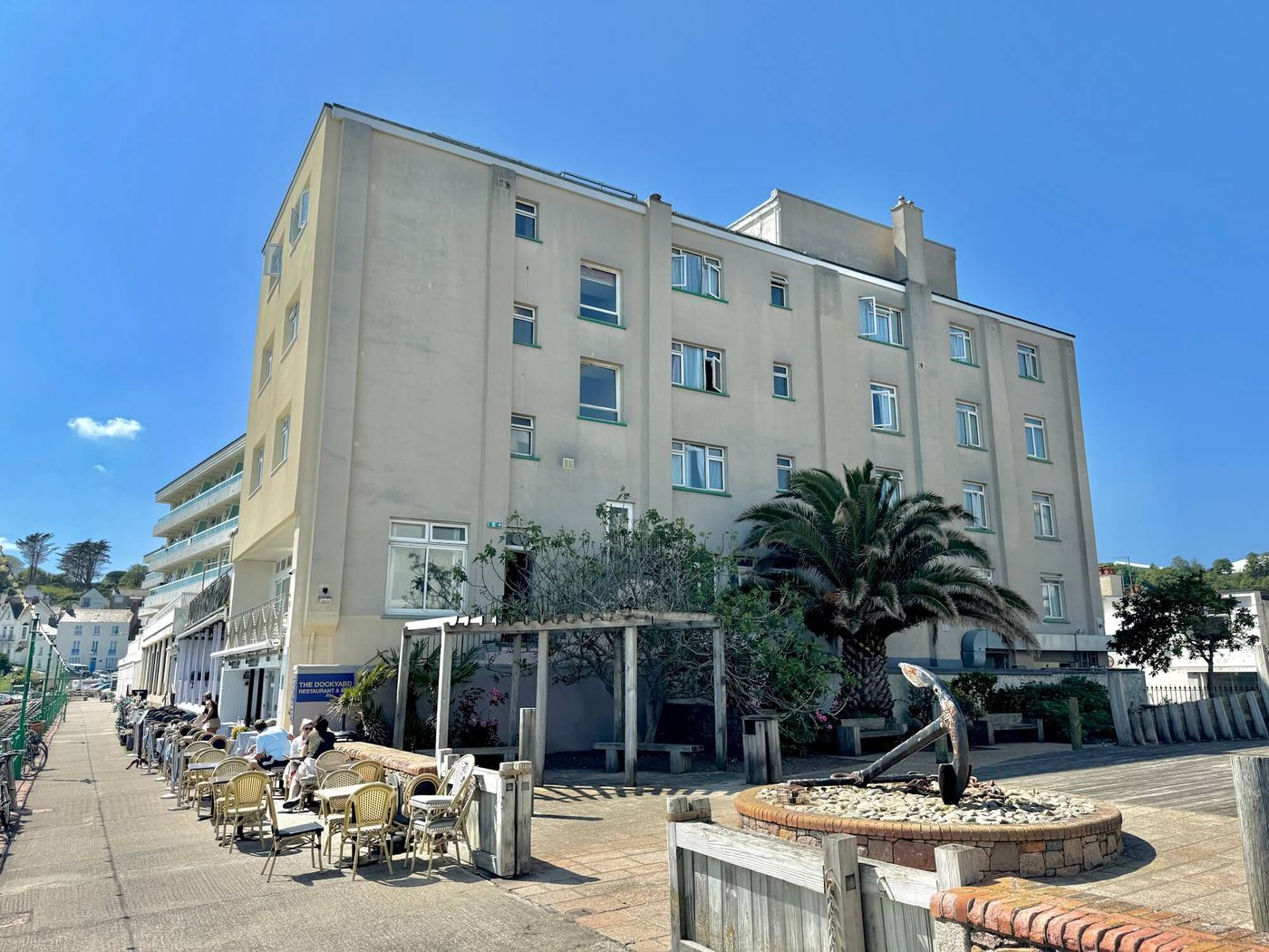 Marina Metro Hotel seen from the promenade at Havre des Pas, St Helier, with tables set out on the seafront terrace and a palm tree beside the entrance